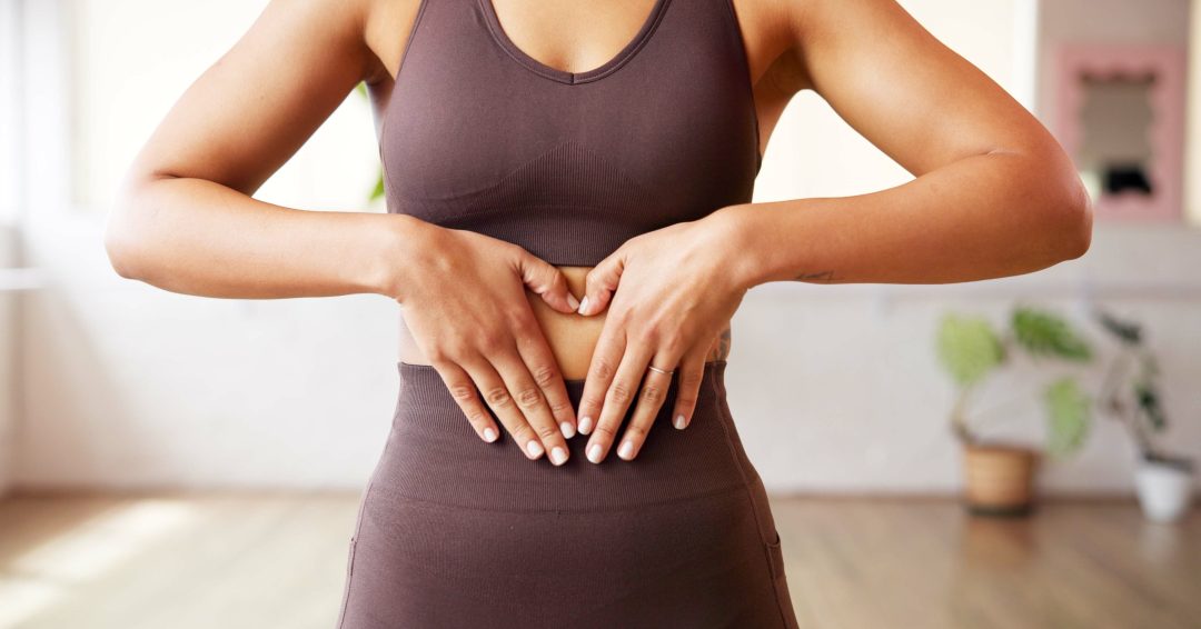 Fitness, heart hands and woman in gym with stomach, gut health and inspiration for body goals. Sport, emoji and athlete in studio with gesture, weight loss and digestive balance in wellness routine